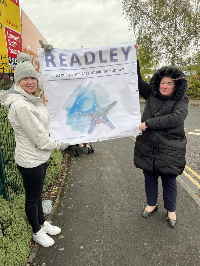 Two women hold a sign for a mesothelioma support group