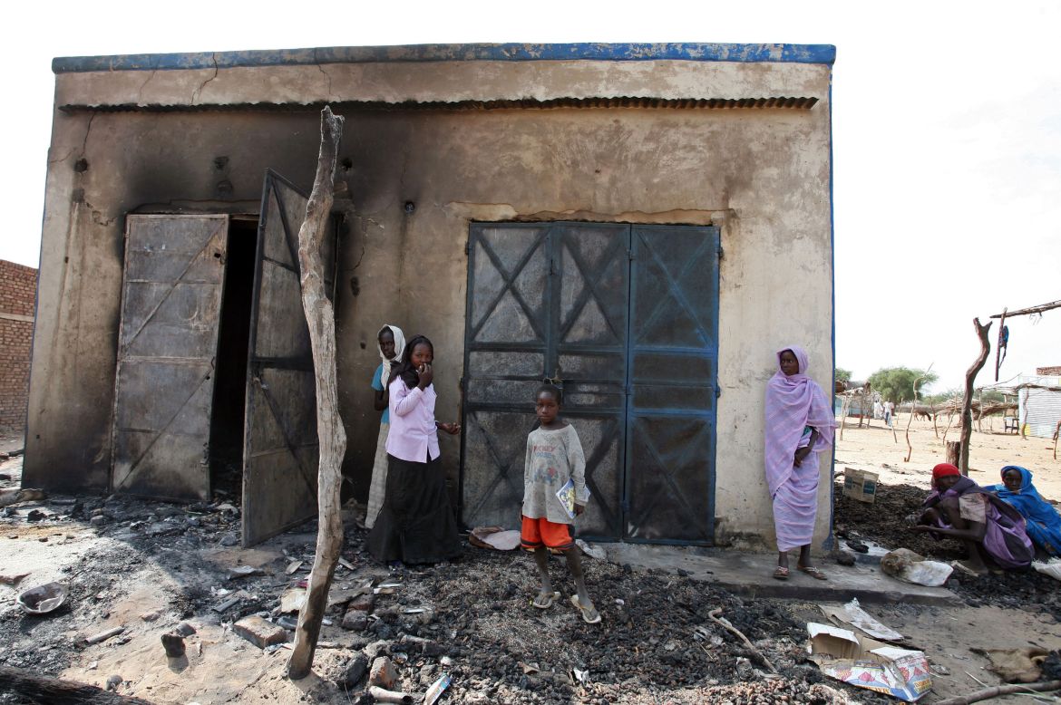 women and children stand in front of burnt out shops