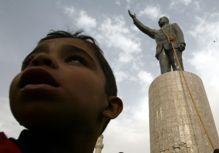 Un joven iraquí se para frente a una estatua del presidente iraquí Saddam Hussein con una soga alrededor del cuello.