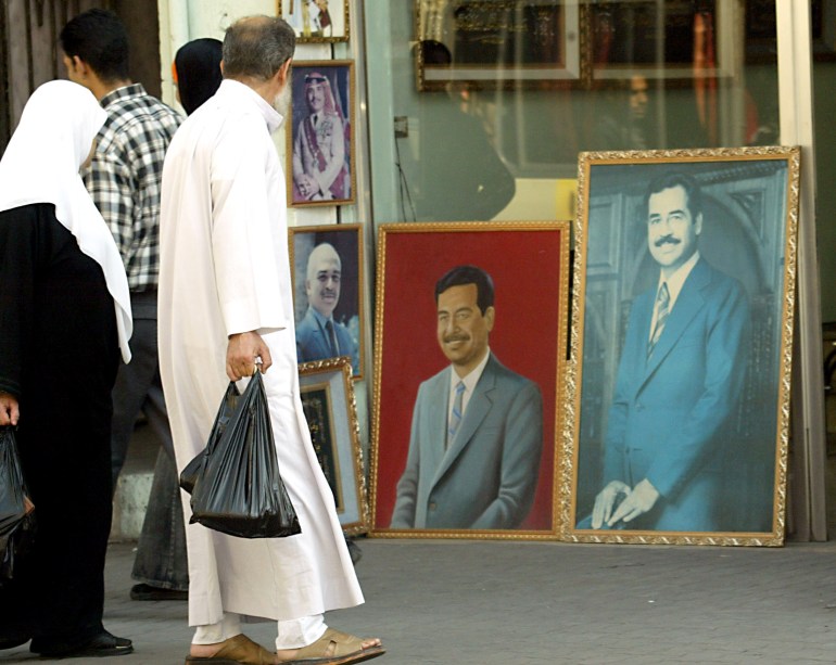 Jordanians pass by posters of ousted Iraqi President Saddam Hussein displayed in a down-town Amman