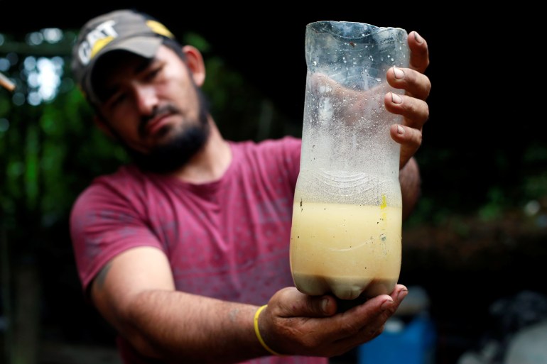A man presents a plastic bottle containing a yellowish liquid.there is sediment on the bottom