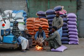 Labourers keep themselves warm near a fire during a cold morning, as they wait for work at the wholesale grain market in Karachi