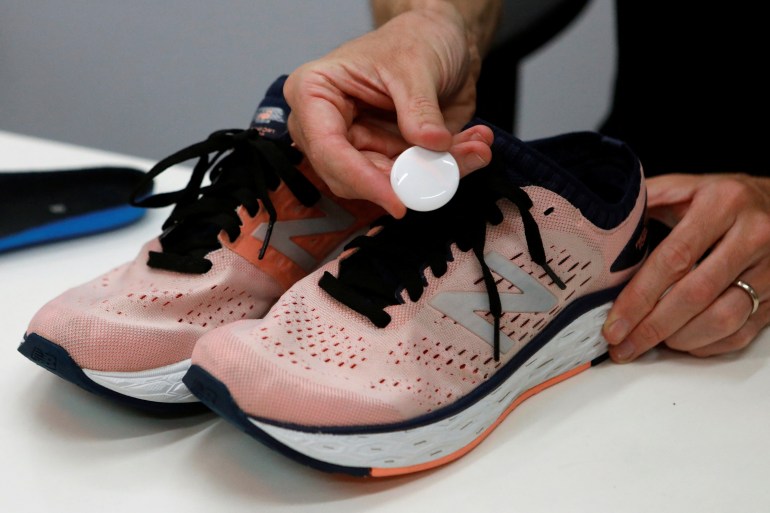 A person holds a flat, round tracking device above a pair of pink sneakers