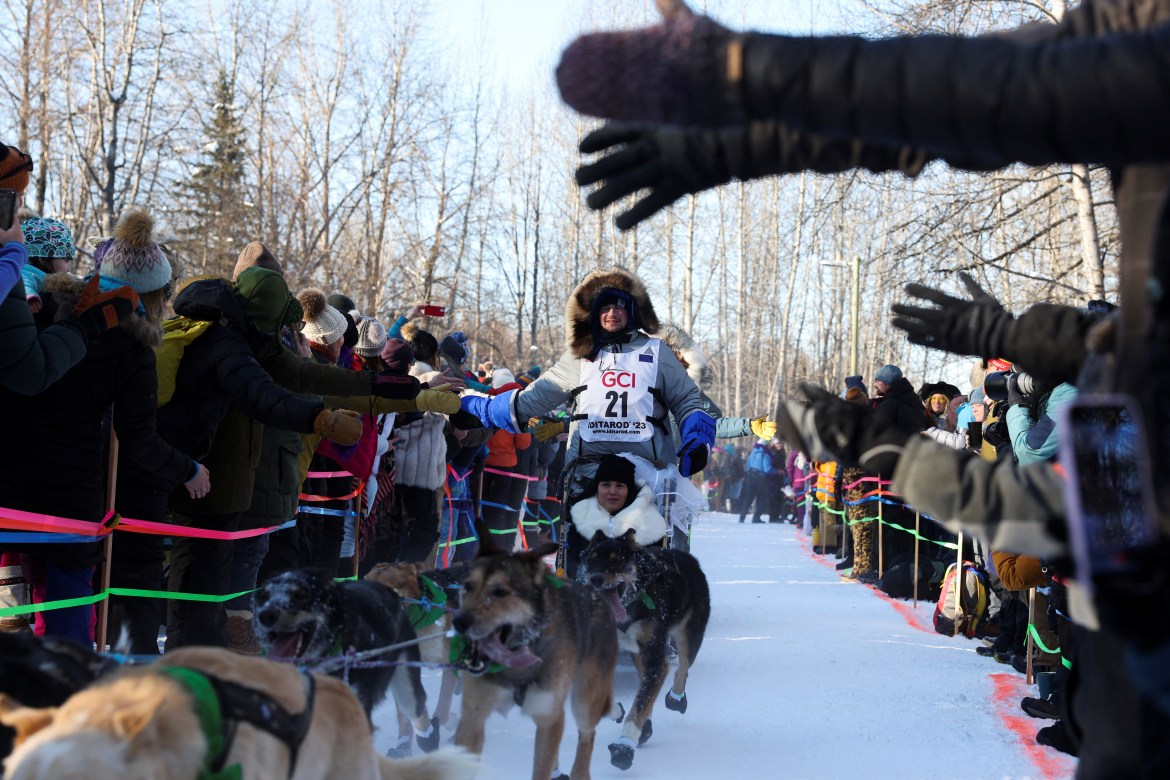A dog sledder gives a high-five to a fan as crowds pack the snowy trail on the Iditarod
