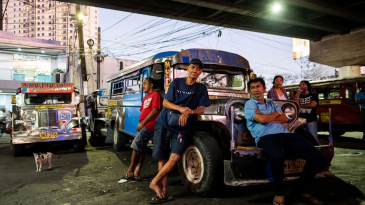 Three jeepney drivers leaning against the bonnet of one of a parked jeepney. It's parked