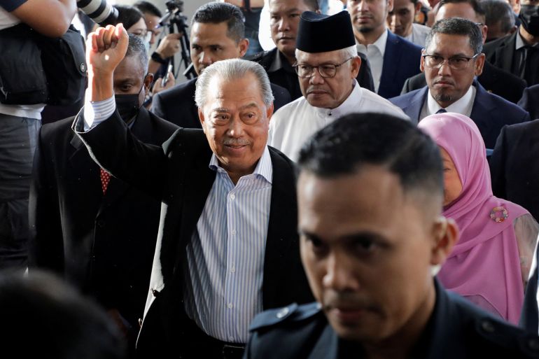 Muhyiddin Yassin punches the air as he arrives at court on Friday morning. There are police in front of him and he is followed by other members of his party.