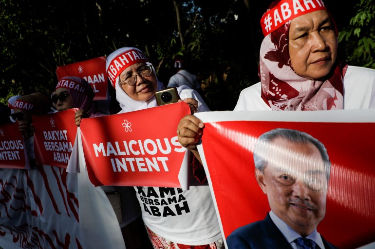 Supporters of Muhyiddin Yassin holding placards reading 'malicious intent' and holding his photo. They are wearing red bandanas reading 'abah' (father)