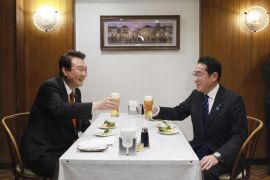 Fumio Kishida (right) and Yoon Suk-yeol toast with a glass of beer during a meal at a Tokyo restaurant. They are sitting opposite each other at a table. There are some appetisers in front of them. They are smiling.