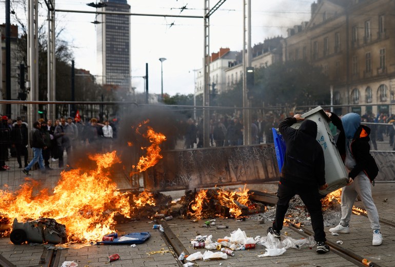 İnsanlar, Fransız Anayasası'nın özel bir maddesi olan 49.3 maddesinin Fransız hükümetinin, milletvekilleri tarafından oylama olmaksızın Ulusal Meclis'ten geçirilmek üzere emekli maaşları reform tasarısını geçirmesini protesto etmek için bir gösteride çıkan çatışmalar sırasında ateşin yanında bir nesne taşıyor. Nantes, Fransa, 18 Mart 2023. REUTERS/Stephane Mahe