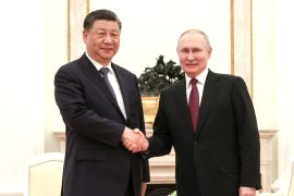 Russian President Vladimir Putin and Chinese President Xi Jinping shake hands while looking at the camera.