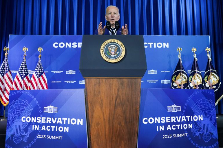US President Joe Biden speaks at a podium, surrounded by signs advertising the Conservation in Action summit.