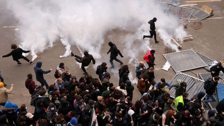 Protesters throw tear gas canisters back amid clashes in Paris on March 23, 2023. Smoke, presumably from gas canisters thrown by police, fills part of the street.