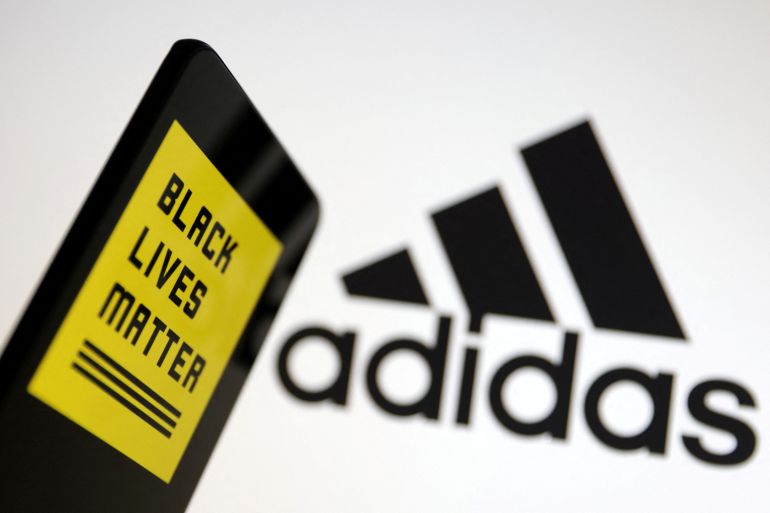 The Black Lives Matter logo in yellow and black, side by side with the Adidas logo. Both use three-stripe logos. For the Black Lives Matter imagery, the three stripes come underneath the name of the organisation. For Adidas, they come above, arranged in a pyramidal shape.