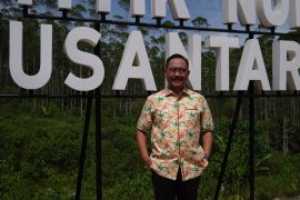 Bambang Susantono, the head of Indonesia's new capital city project, poses for a portrait. He is wearing a batik shirt, has his hands in his pockets and looks relaxed. The Nusantara sign is behind him.