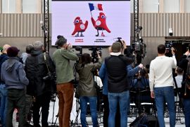 Journalists film a picture of France 2024 Olympics mascots on a billboard