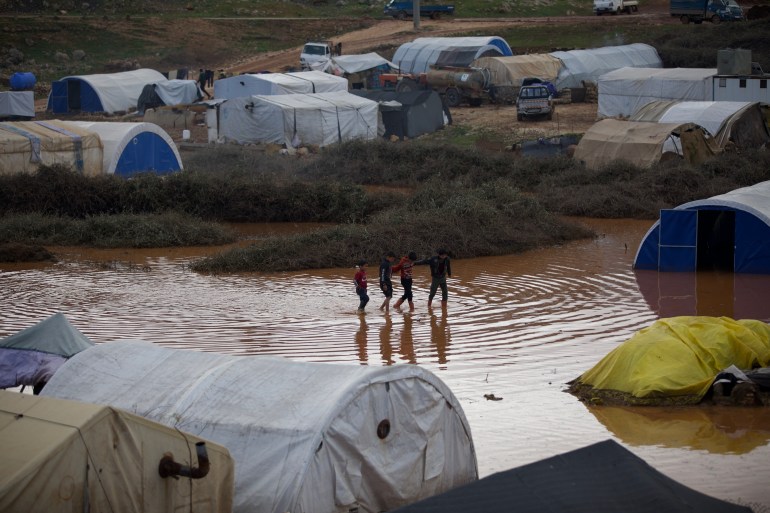 Children wade in a pool of dirty water following torrential rains that hit the camps of newly housed earthquake survivors in Syria