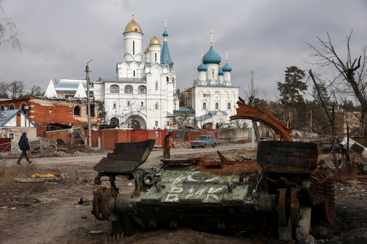 A local resident walks past a damaged church and a destroyed Russian tank in the town of Svyatogirsk