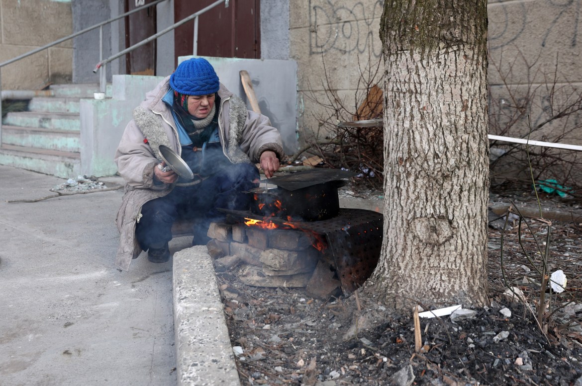 A local elderly woman cooks outside a residential building in the town of Bakhmut, in the Donetsk region