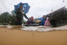 A family walking through brown flood water in a street in the town of Yong Peng in southern Malaysia. They have umbrellas.