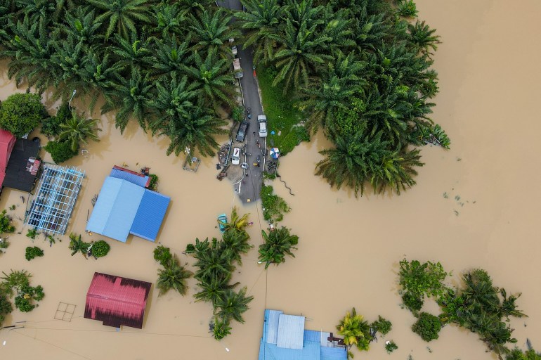 An aerial view of a flooded roads and houses in Yong Peng in the south of Malaysia. There are some trees and a few houses visible through the brown flood waters.