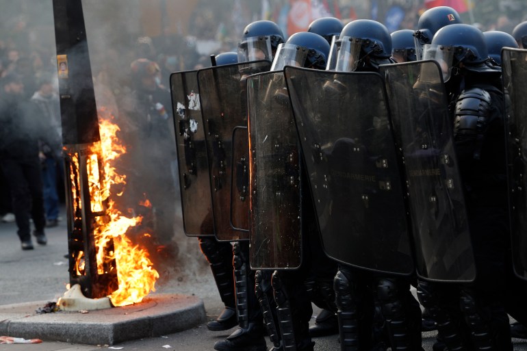 French gendarmes in riot gear operate next to a burning urban element during a demonstration in Paris on March 7, 2023, on the sixth day of nationwide rallies organized since the start of the year against French President's pension reform and its postponement of the legal retirement age from 62 to 64.