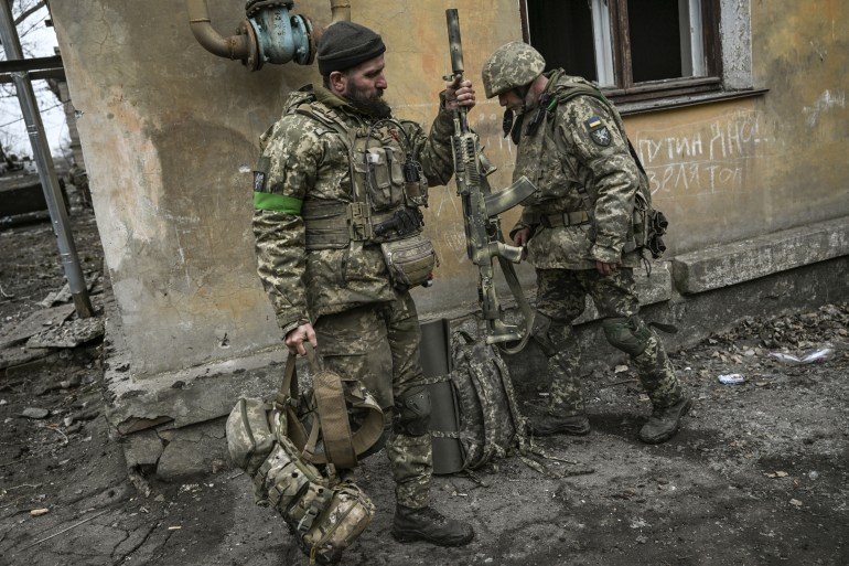 Two Ukrainian servicemen prepare to join the front line in Bakhmut, Ukraine. One is holding a rifle and both have medium-sized packs of military kit.