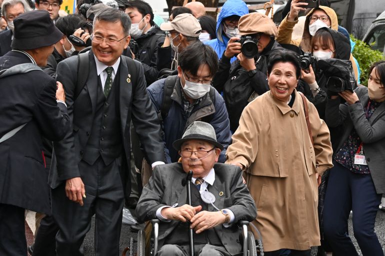 하카마다 이와오가 가족 및 지지자들과 함께 도쿄 법정에 출석합니다.  그는 휠체어입니다.  그리고 안경을 쓴 그의 여동생이 그의 옆에 있고 그녀가 걷고 있는 동안 미소를 짓고 있습니다.