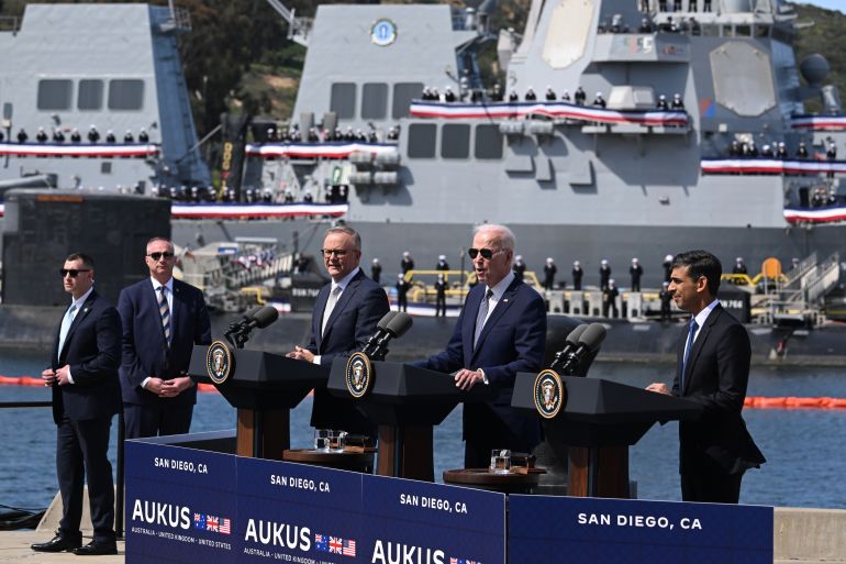 Australian PM Anthony Albanese, US President Joe Biden and UK Prime Minister Rishi Sunak standign at lecterns at a San Diego naval nase. Biden is speaking. There are two secret service agents nearby and a submarine and navy ship moored behind them with their crew standing to attention on deck.