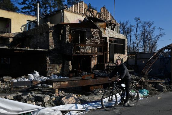A cyclist rides on a bicycle past a house destroyed by shelling.