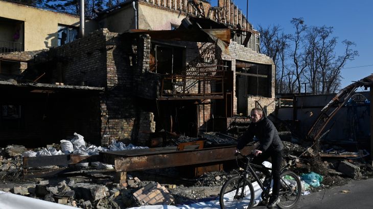 A cyclist rides on a bicycle past a house destroyed by shelling.