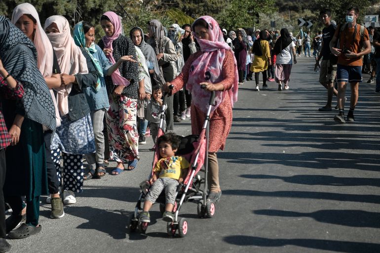 Asylum seekers queue for food distribution along the roadside where thousands are living with out shelter and exposed to the elements following the burning down of their camp, near the Kara Tepe camp on the island of Lesbos on September 13, 2020. - Over 11,000 people -- including some 4,000 children -- have been sleeping rough since the notoriously overcrowded and unsanitary camp of Moria burned down this week..Aided by army bulldozers, work crews have worked round-the-clock to erect a makeshift camp for 3,000 people a few kilometres from the ruins of Moria where the first 500 refugees are already accomodated. (Photo by LOUISA GOULIAMAKI / AFP)