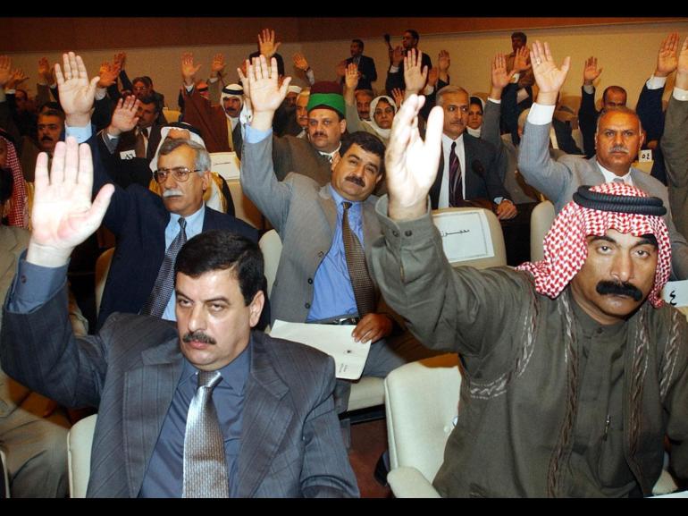 Iraq members of parliament with arms raised to vote