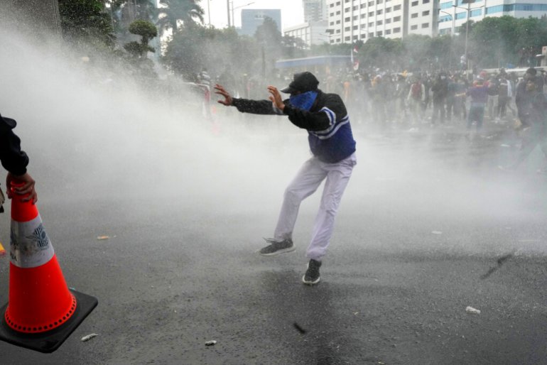 A student reacts as police use a water cannon to disperse protesters during a rally outside the parliament in Jakarta, Indonesia, Monday, April 11, 2022. Thousands of students marched in cities around Indonesia on Monday to protest against rumors that the government is considering postponing the 2024 presidential election to allow President Joko Widodo to remain in office beyond the two-term legal limit, calling it a threat to the country's democracy. (AP Photo/Tatan Syuflana)