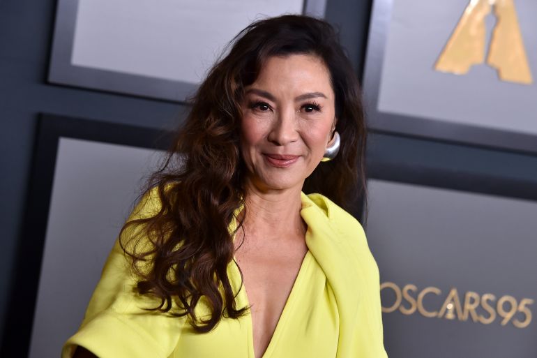 Michelle Yeoh pictured at an Oscar's event. She's wearing a yellow evening gown and smiling.