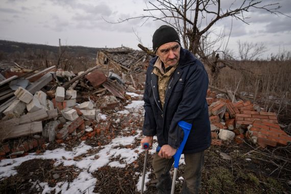 Andrii Cherednichenko, 50, who was injured after stepping on a land mine, stands with the aid of crutches in front of the ruins of his home, in Kamyanka, Ukraine. He seems bitter as he looks away.