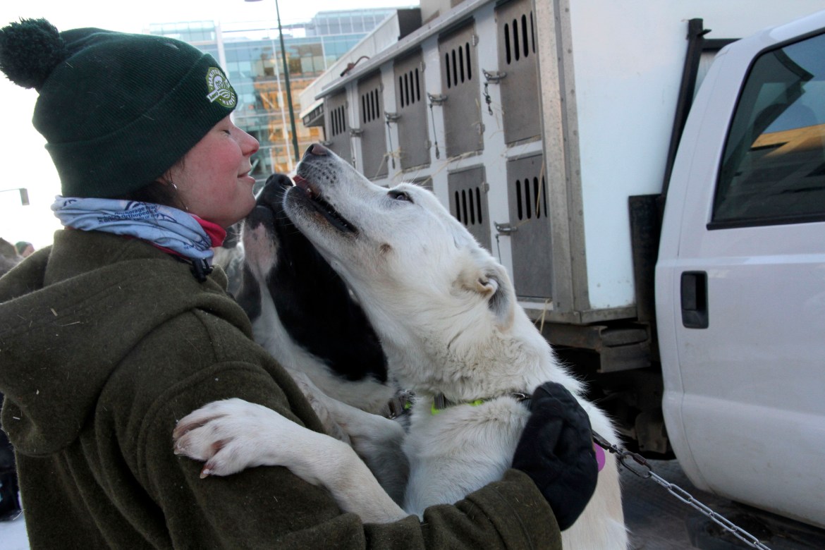 A white dog puts its front paws on a woman's shoulders and gives her a big lick in the face