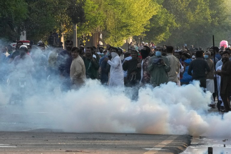 Susținătorii fostului prim-ministru pakistanez Imran Khan se acoperă în timp ce poliția trage cu gaze lacrimogene.