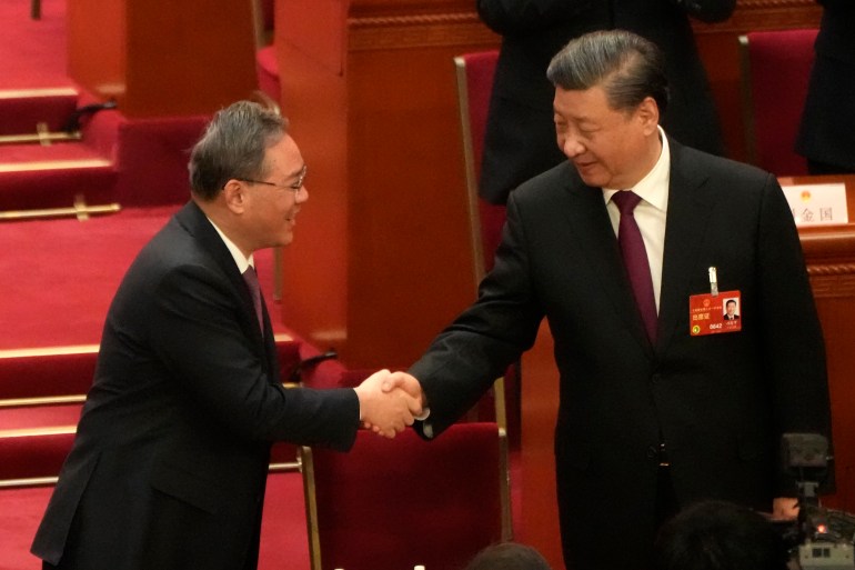 Xi Jinping and Li Qiang shake hands and smile. 