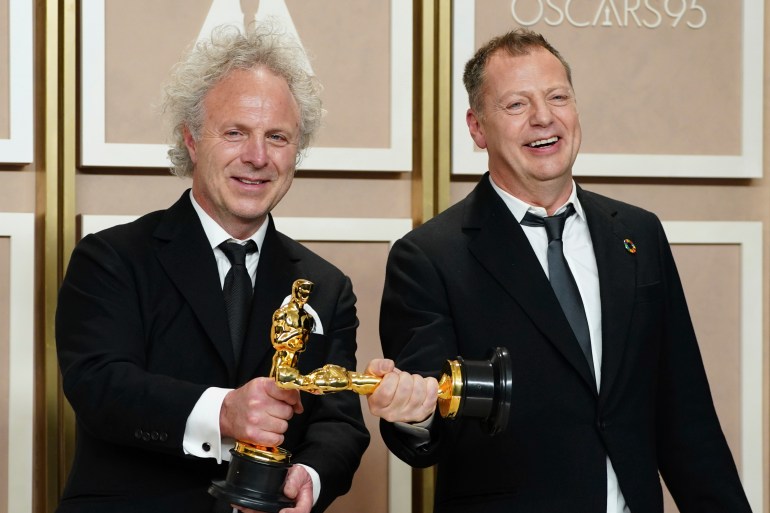 Two men hold their Oscars perpendicular to one another
