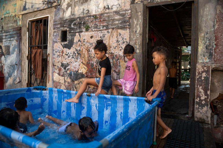 Crianças se amontoam em uma piscina de plástico azul do lado de fora de uma casa