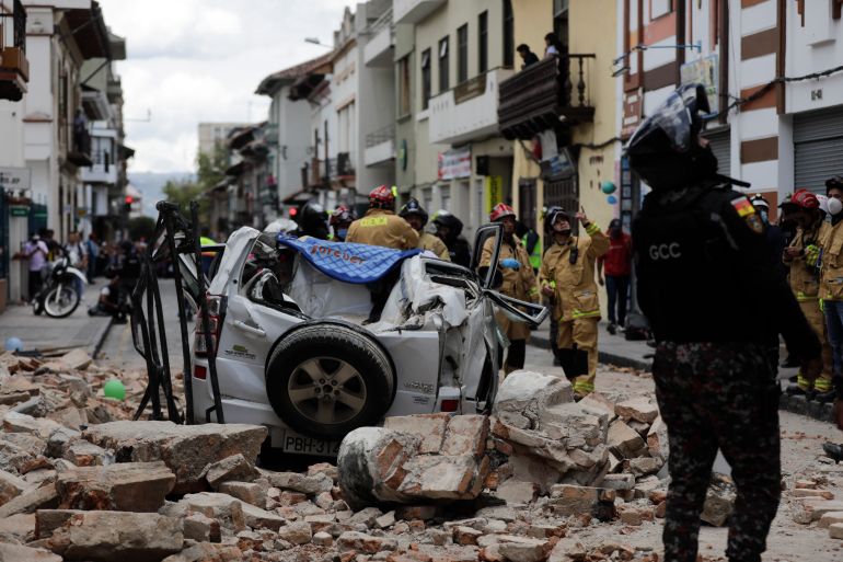A police officer looks up next to a car crushed by debris after an earthquake shook Cuenca, Ecuador, Saturday, March 18, 2023. The US Geological Survey reported an earthquake with a magnitude of 6.7 on Saturday about 80 kilometres (50 miles) south of Guayaquil, Ecuador.