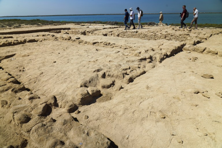 Archeologen en journalisten lopen langs ruïnes die zijn opgegraven op het eiland al-Siniyah in Umm al-Quwain, Verenigde Arabische Emiraten, maandag 20 maart 2023. Archeologen zeiden maandag dat ze de oudste parelstad in de Perzische Golf hebben gevonden op een eiland voor een van de de noordelijke sjeikdoms.  Verenigde Arabische Emiraten.  (AP Foto/Jon Gambrell)