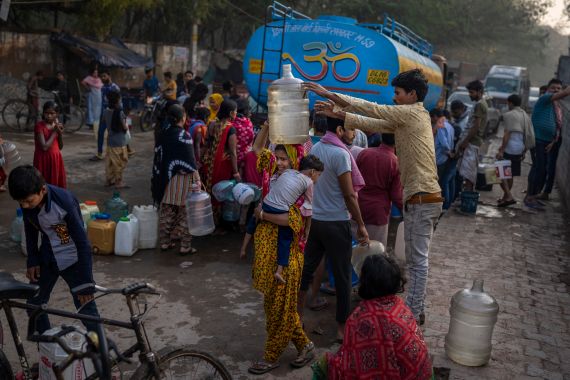 A woman balances a water can on her head while carrying a child as people collect water from a mobile water tanker on World Water Day in a residential area in New Delhi, India