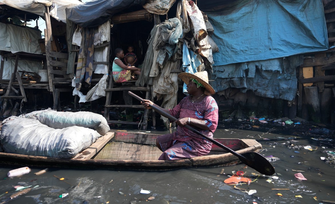 A woman paddles through water surrounded by garbage in a floating slum of Makoko, in Lagos, Nigeria