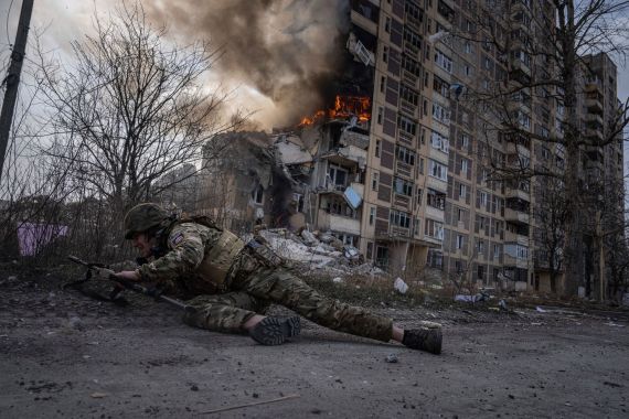 A Ukrainian officer takes cover in front of a burning building