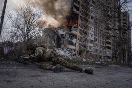 A Ukrainian police officer takes cover in front of a burning building that was hit in a Russian air strike in Avdiivka, Ukraine [Evgeniy Maloletka/AP]