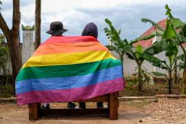 A gay Ugandan couple cover themselves with a pride flag as they pose for a photograph in Uganda on Saturday, March 25, 2023 [AP Photo]