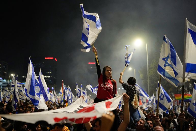 Hundreds of Israeli protesters, many holding flags of Israel over their heads, block a highway in Tel Aviv, Israel.