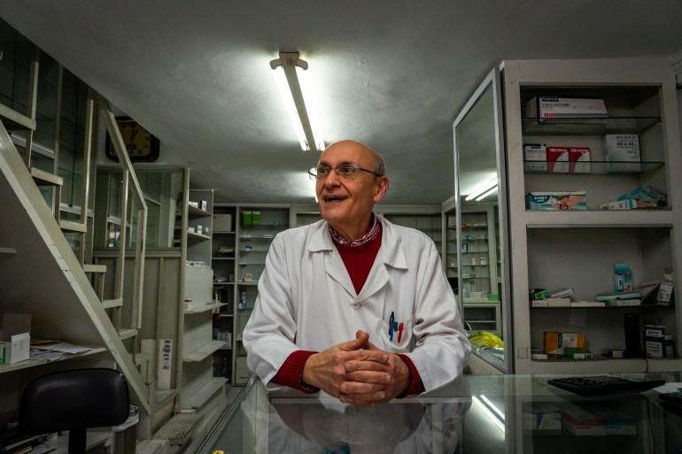 Pharmacist in white lab coat stands behind a counter. 