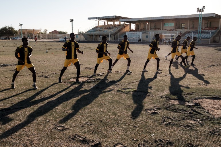 Players at Nassara Football Club stretch and run in unison to warm up before a training session on an old astro pitch at Agadez Stadium [Guy Peterson/Al Jazeera]